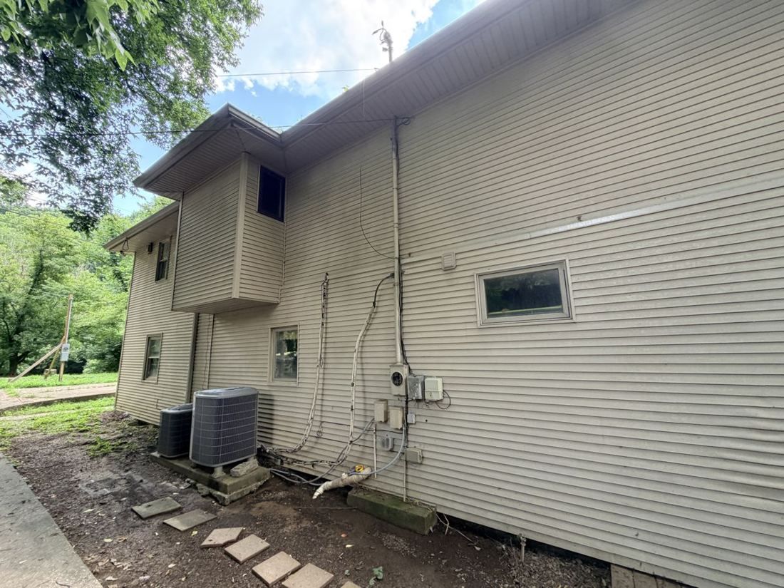 Side elevation of a property during site assessment showing the existing HVAC condenser and utility runs